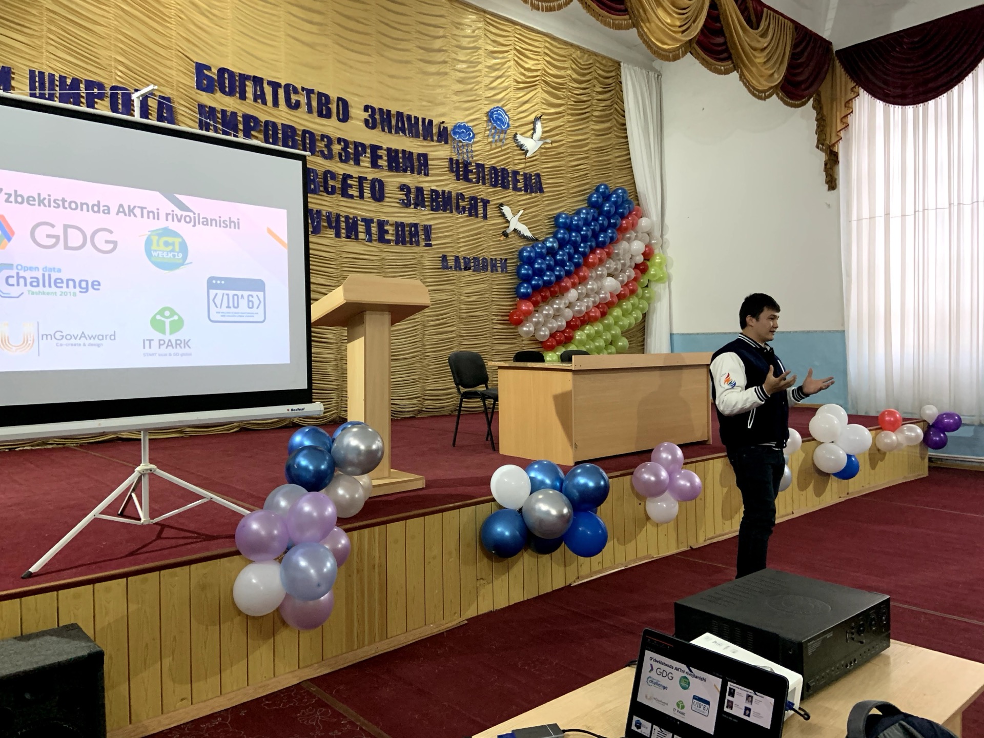 Khurshid Normurodov presenting on stage at an ICT Week conference, with GDG, IT Park and mGovAward logos on screen