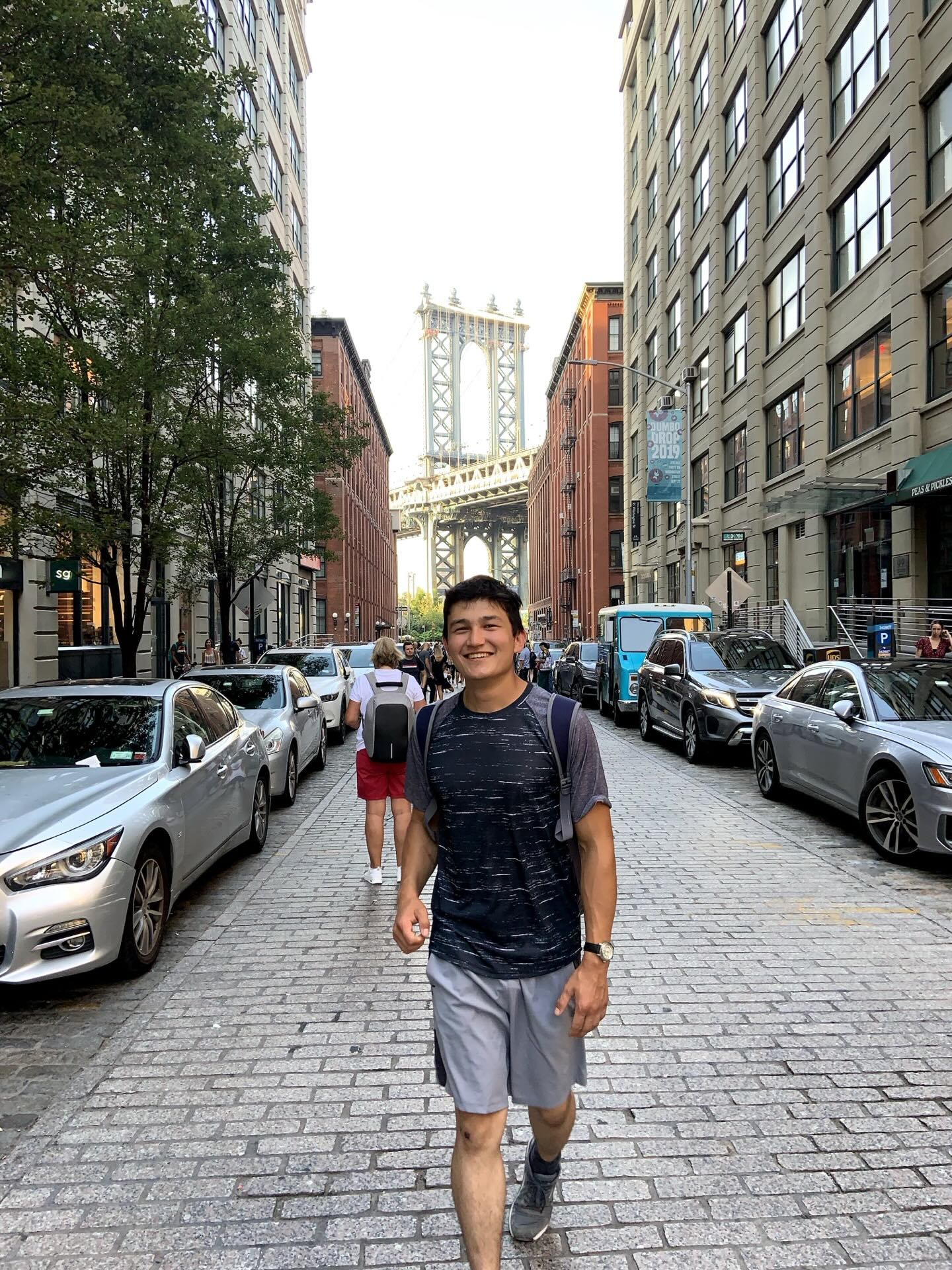Khurshid Normurodov walking through DUMBO, Brooklyn, with the Manhattan Bridge in the background